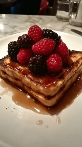 French Toast served with fresh berries and a drizzle of maple syrup on a white plate