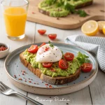 Two slices of whole-grain avocado toast topped with creamy mashed avocado, poached eggs, cherry tomatoes, and red pepper flakes on a ceramic plate.
