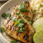 Top-down photo of juicy cilantro lime chicken breasts garnished with fresh cilantro and lime wedges on a rustic white platter.