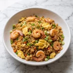 Shrimp and egg fried rice served in a white dish with green onion
