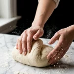 Hands kneading dough by hand on a floured marble surface